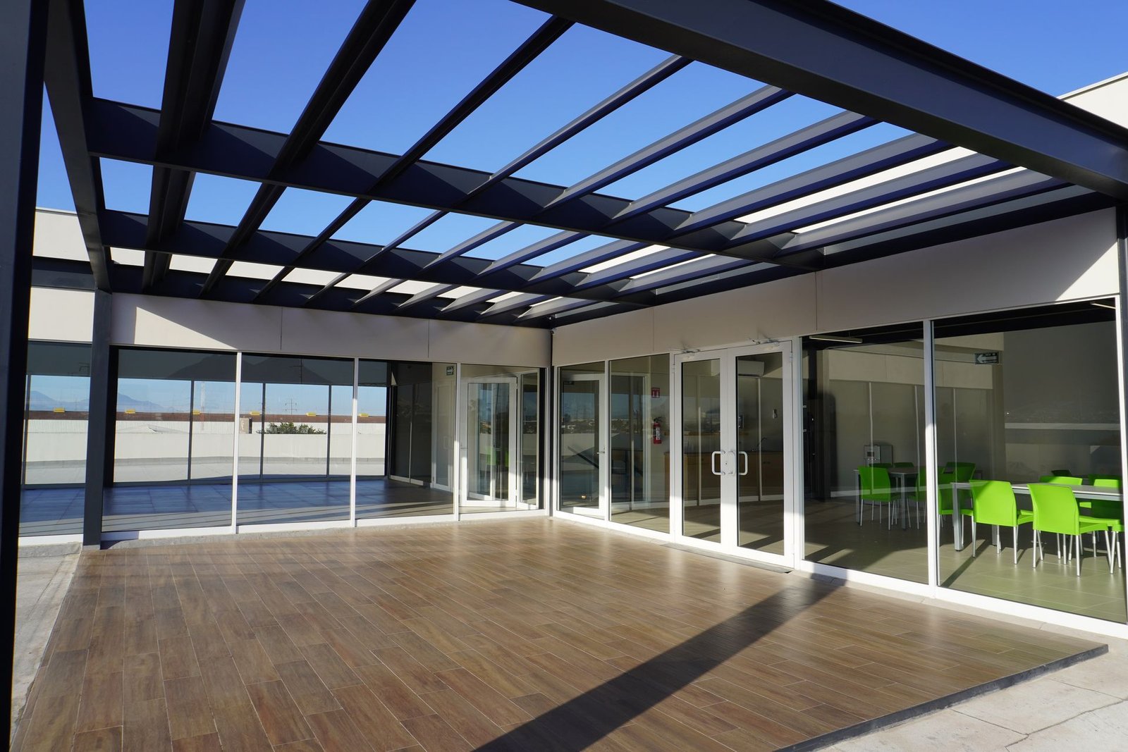 Terraza de oficinas en Monterrey con pérgola de acero y cancelería corrediza de aluminio con cristal templado